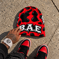 Red and black cow print B.A.E. beanie flat lay with matching red and black streetwear sneakers and male hand.