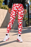 A female wearing red and white Cow patterned leggings, a black sweatshirt, and white sneakers with red accents, standing outdoors on a concrete walkway