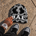 Gray and black cow print B.A.E. beanie made from stretch polyester spandex, featuring distressed Build An Empire graffiti lettering, unisex streetwear styling, and a bold all-over print design.