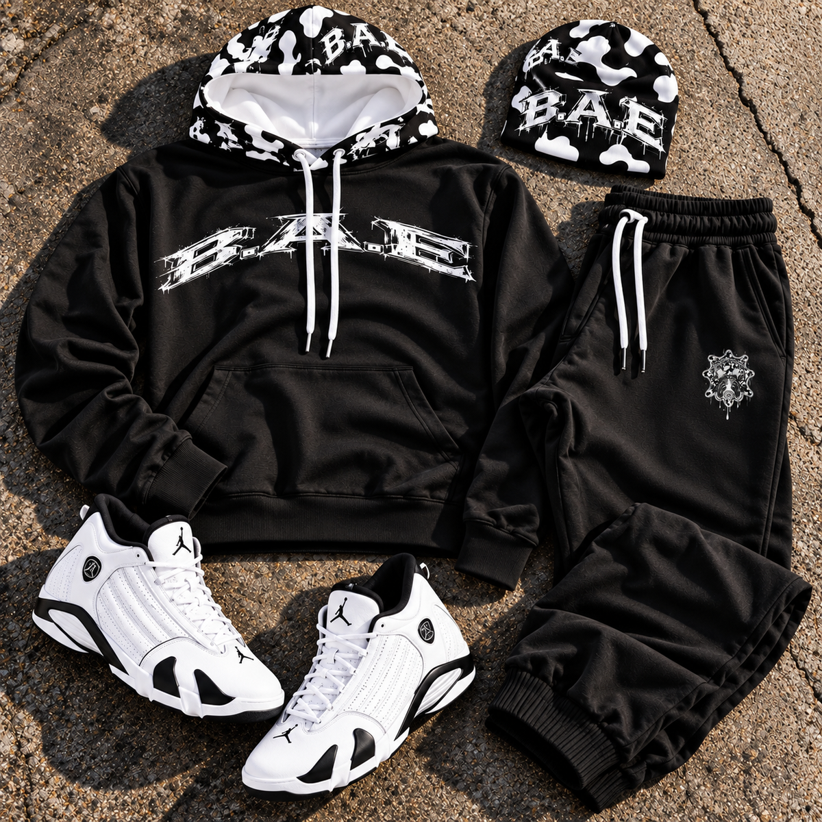 Black B.A.E. entrepreneur streetwear hoodie and jogger set with white B.A.E. chest graphic, black-and-white cow-print hood, matching B.A.E. beanie and white sneakers, styled as a complete urban streetwear outfit.