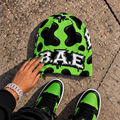 Green and black cow print B.A.E. beanie made from stretch polyester spandex, featuring distressed Build An Empire graffiti lettering, unisex streetwear styling, and a bold all-over print design.