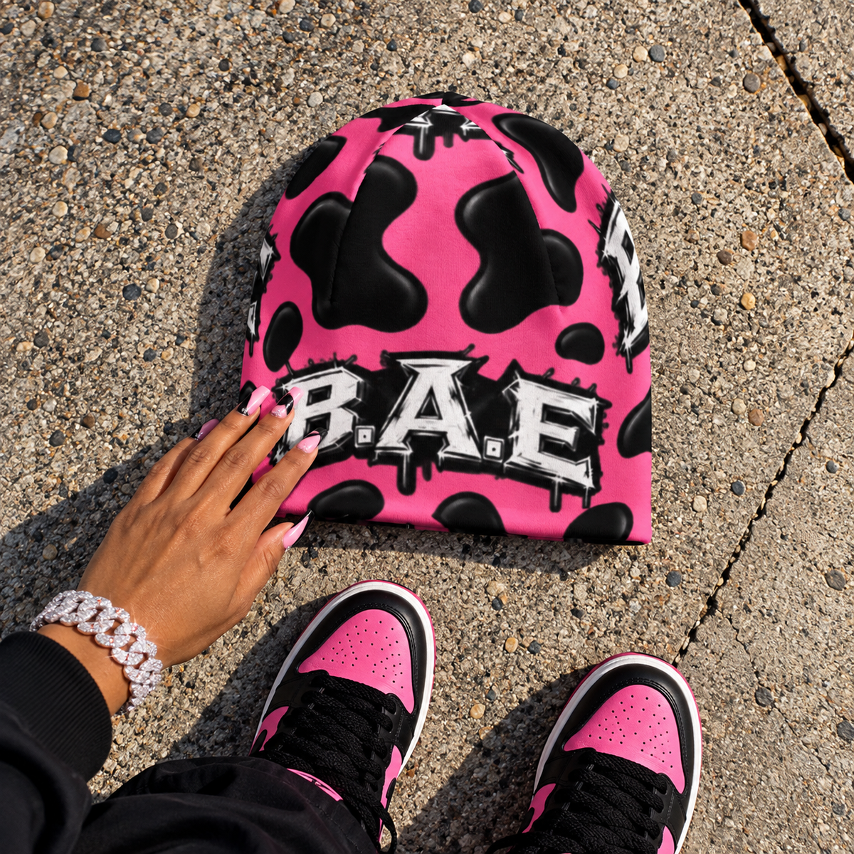 Flat-lay product image
Pink and black cow print B.A.E. beanie flat lay with matching pink and black streetwear sneakers and female hand.