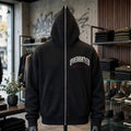 A Trendy black full zip-up hoodie displayed on a mannequin inside a retail store. The hoodie features a white arched 'OVERRATED' text graphic and a small red Millions Pending script accent on the left chest