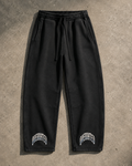 Premium black vintage wash streetwear sweatpants flat lay featuring heavyweight 390 GSM fleece, oversized barrel-leg fit, elastic drawstring waist, side pockets, structured panel detailing, and OVERRATED typography near the cuffs. Exclusive streetwear jogger pants designed for fall and winter outfits, sneaker styling, and the NFEO OVERRATED Collection.