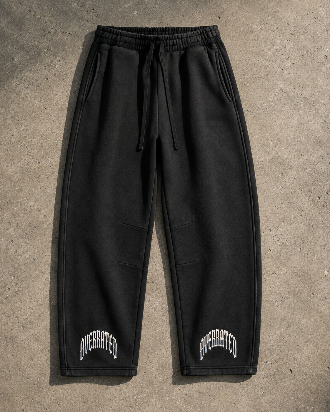 Premium black vintage wash streetwear sweatpants flat lay featuring heavyweight 390 GSM fleece, oversized barrel-leg fit, elastic drawstring waist, side pockets, structured panel detailing, and OVERRATED typography near the cuffs. Exclusive streetwear jogger pants designed for fall and winter outfits, sneaker styling, and the NFEO OVERRATED Collection.