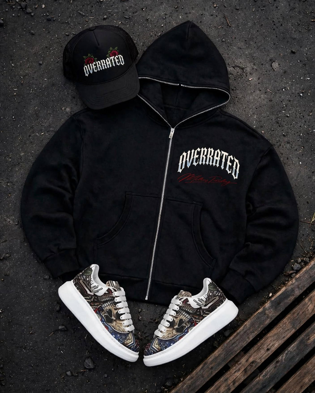FRONT view of a Trending premium black Full zip-up hoodie laid flat on a dark textured surface, featuring a large graphic print on the Front Left chest with the word OVERRATED. arched with an red Millions pending signature script Showing Full Overrated collection foam Trucker hat, plus McQueen Graffiti style Platform Sneakers 