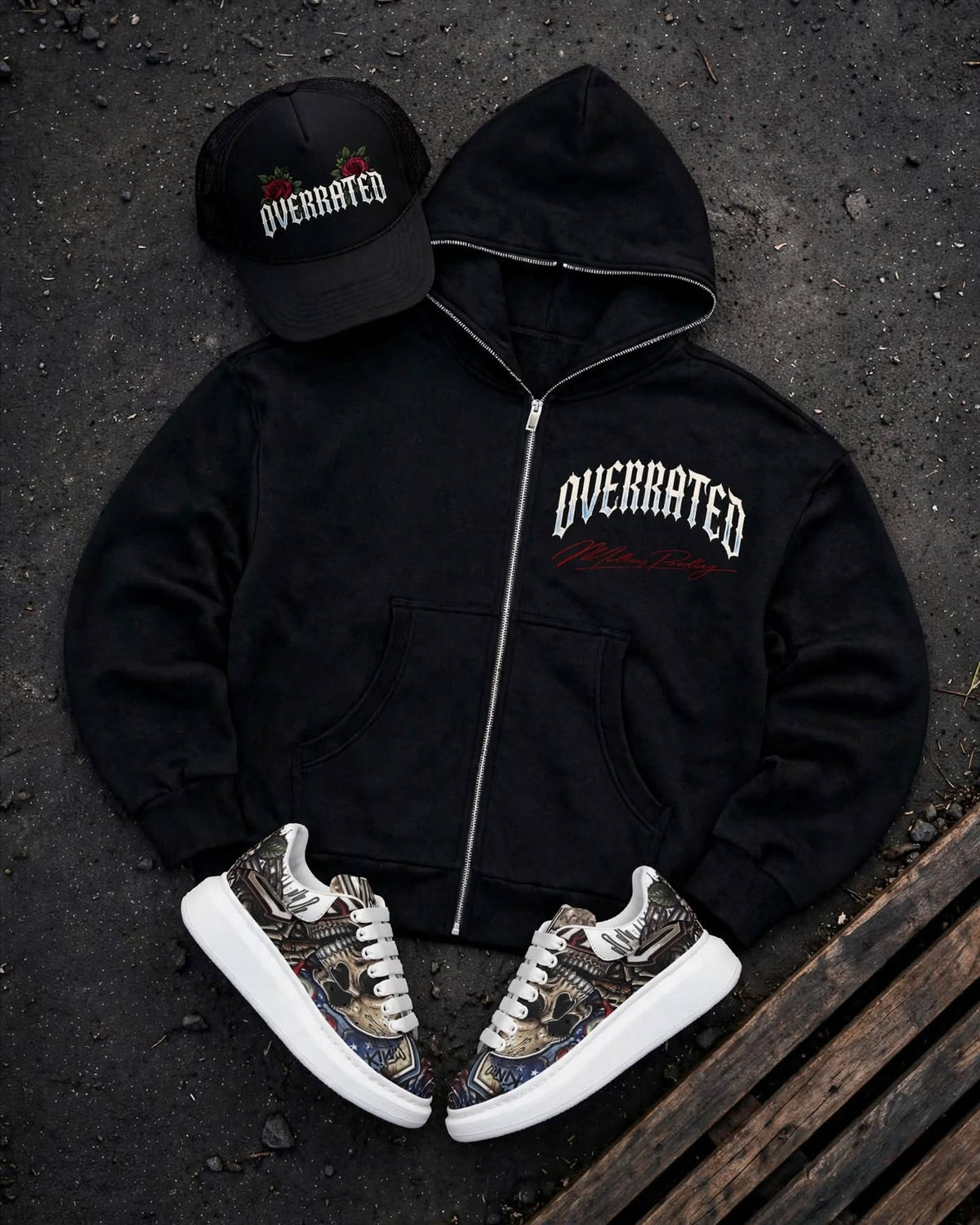 FRONT view of a Trending premium black Full zip-up hoodie laid flat on a dark textured surface, featuring a large graphic print on the Front Left chest with the word OVERRATED. arched with an red Millions pending signature script Showing Full Overrated collection foam Trucker hat, plus McQueen Graffiti style Platform Sneakers 